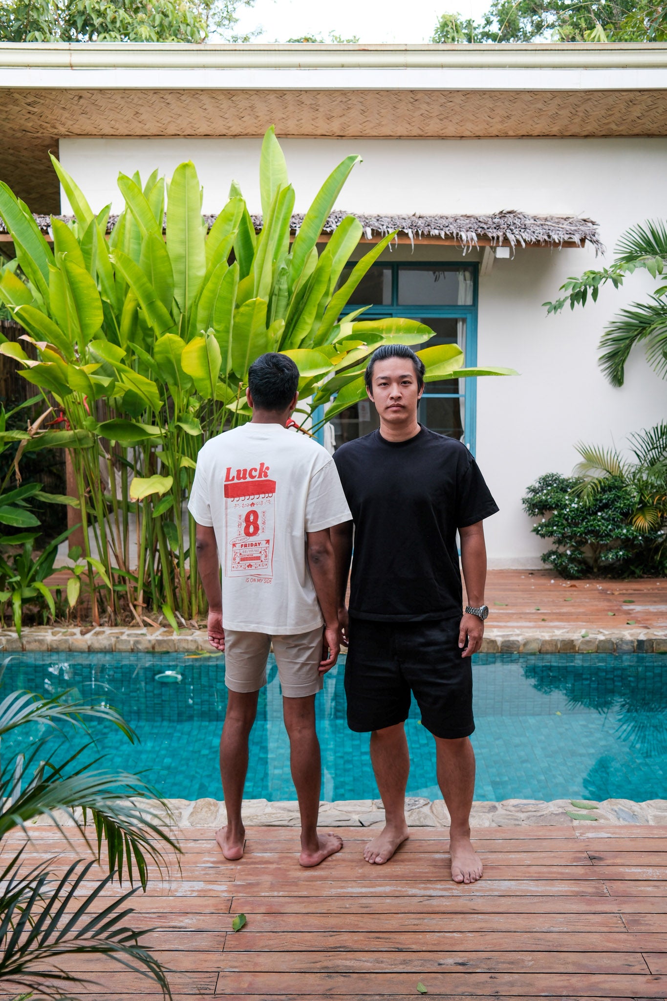 Two men standing by a pool with lush greenery and a house in the background